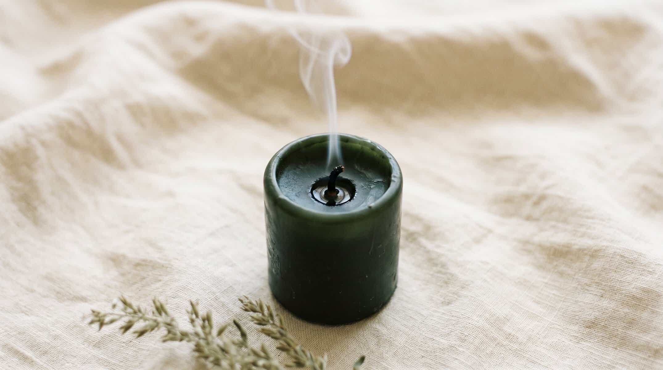 Green aromatherapy candle with smoke rising, on beige fabric background.